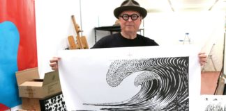 John Van Hamersveld Has Endless Visions JVH Man in a hat and glasses holding up black and white wave artwork