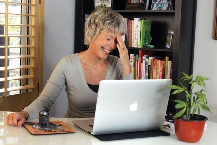 middle age married woman laughing over laptop with cannabis plant in foreground