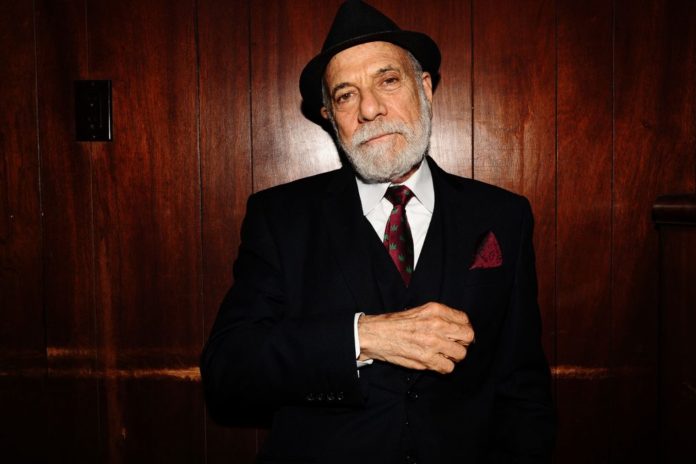 older dapper man with hat and beard in suit wearing a red weed tie