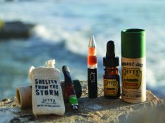 Jetty Extracts Fights Cancer While Meeting High Demand collection of cannabis vape pens, oils, and extracts on stone in front of ocean