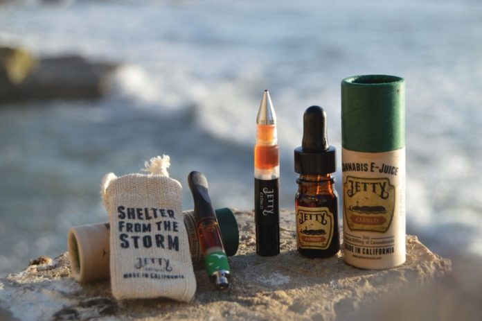 collection of cannabis vape pens, oils, and extracts on stone in front of ocean
