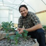 Jonathan Valdman is Forever Flowering young man in plaid shirt smiling next to young cannabis plants in grow bags