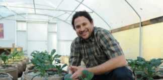 Jonathan Valdman is Forever Flowering young man in plaid shirt smiling next to young cannabis plants in grow bags