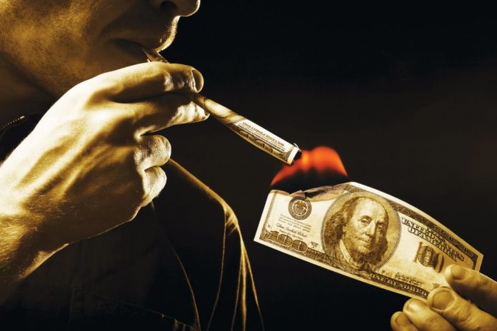 man burning hundred dollar bill and smoking hundred dollar joint