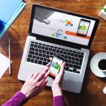 MyDX Brings Cannabis Lab Testing to the Masses woman holding mydx app on phone with a computer and coffee cup on the table