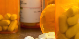 Medical Cannabis Continues the Case Against Opiates white pills with center etching on table surrounded by orange medicine containers