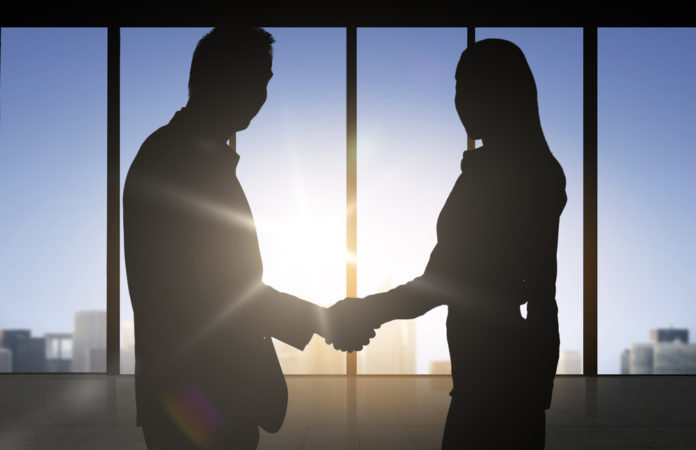 man and woman professionals shaking hands in front of city skyline