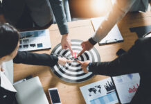 High Finance: What Makes a Good Acquisition Target? Executives pointing to acquisition target by sutadimages mg Magazine