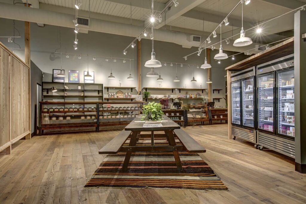 intnerior of a dispensary with wood floor and a wooden picnic table in the center of the room display cases line the walls and lights hang from the ceiling 