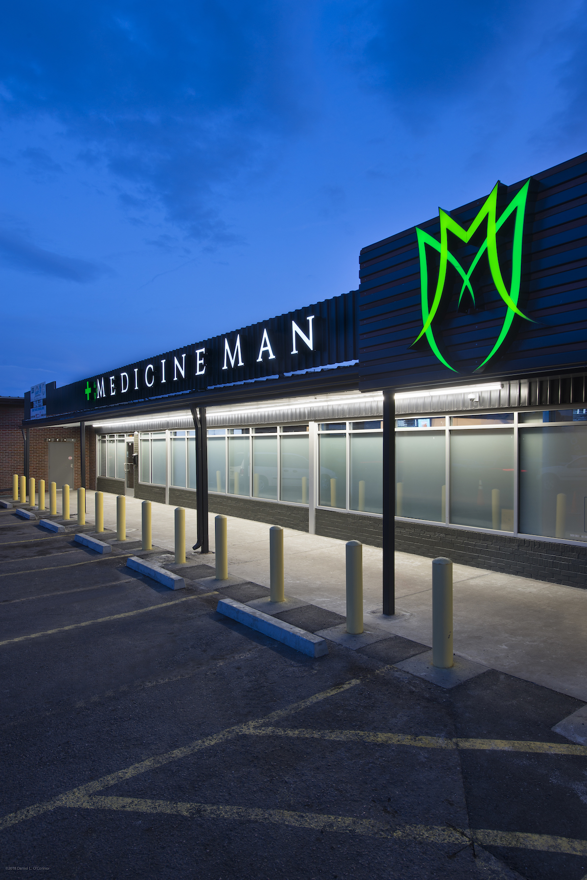 outside a dispensary at dusk building is black with green light up flower logo