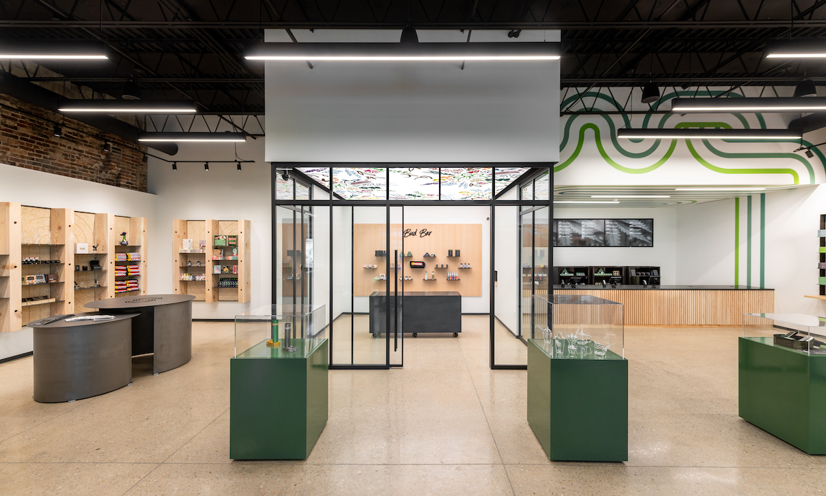 dispensary interior with wood floors and black ceilings and green display tables throughout the room
