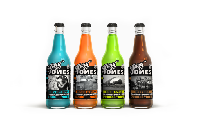 four glass bottles of mary jones soda lined up next to one another one is turqoise and labeled berry lemonade, one is orange and labeled orange and cream, one is lime green and labeled green apple, and one is brown and labeled root beer. The Mary Jones logo sticks out prominently in black and white bold letters on each bottle