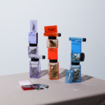 Miss Grass Announces Purposeful Rebrand and Five New SKUs product display of Miss Grass flower a rolled join lays on a table in front of three stacks of weed filled jars, one purple, one red, and one blue