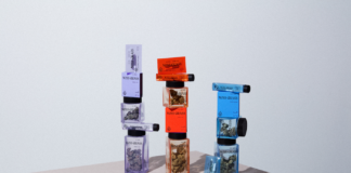 Miss Grass Announces Purposeful Rebrand and Five New SKUs product display of Miss Grass flower a rolled join lays on a table in front of three stacks of weed filled jars, one purple, one red, and one blue