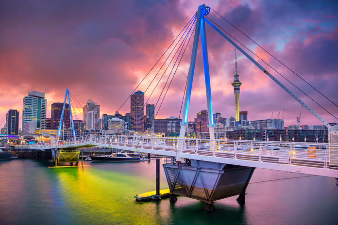 an image of New Zealand urban coastline during a dramatic pink sunset the city is in the background and in the foreground in the water and an illuminated bridge general vibe is futuristic and inspiring