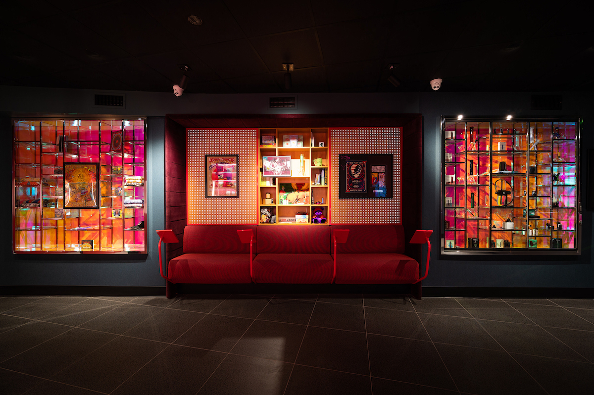 a red couch in the center of a wall filled with cannabis memorabilia illuminated from within the wall