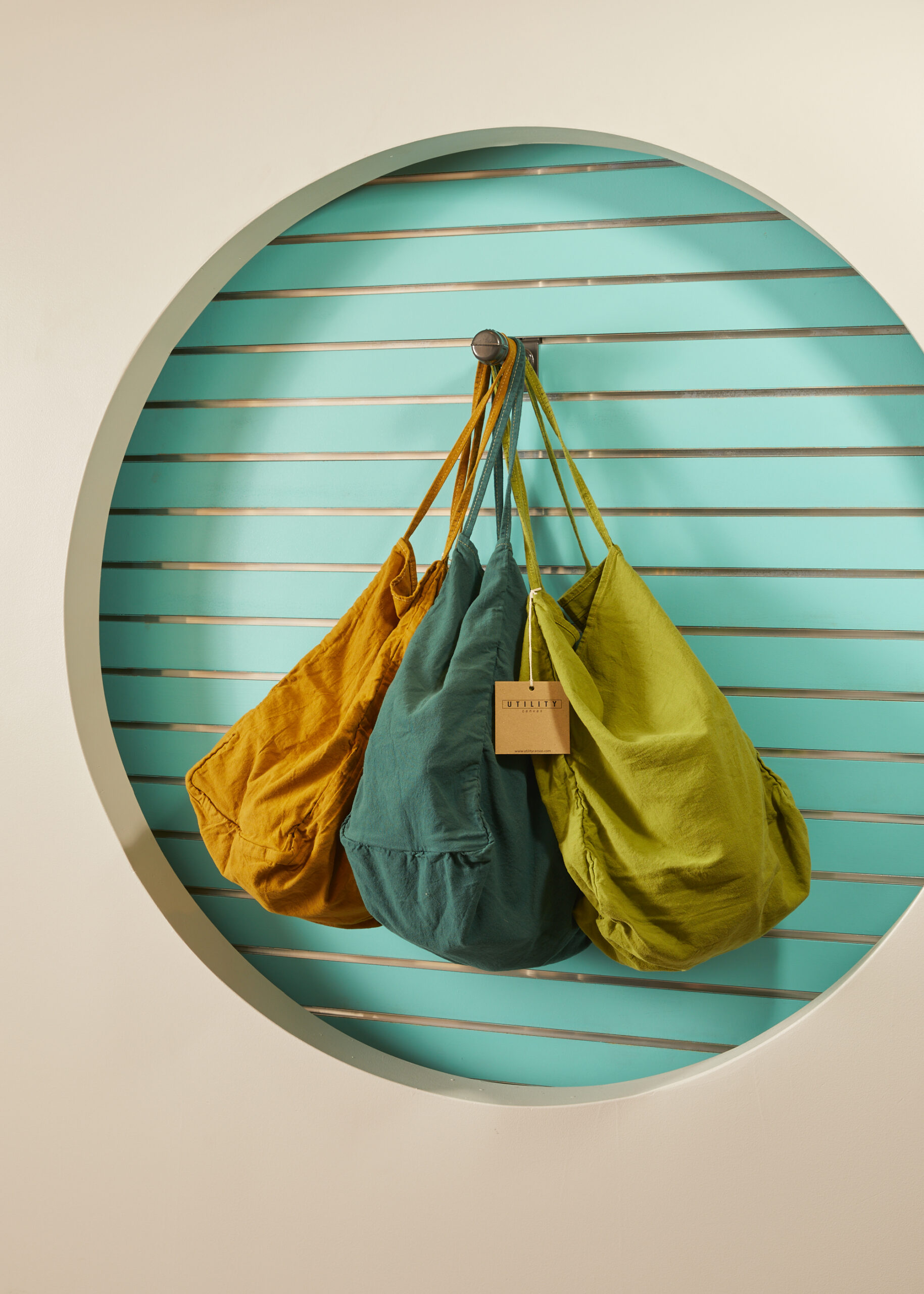 a white wall with a circle cutout revealing a teal wallpaper displaying three canvas bags in orange green and gold