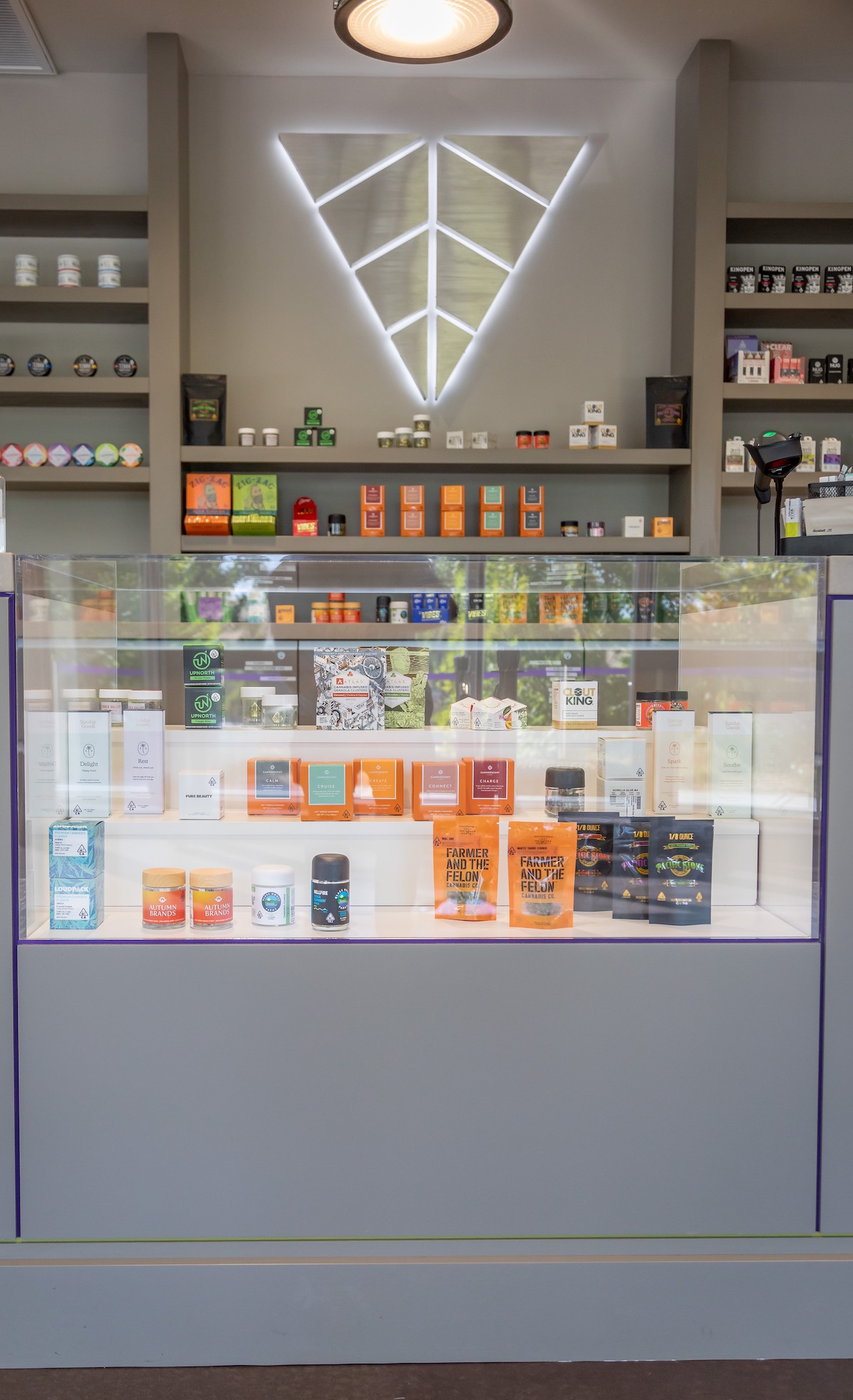 dispensary display cases embedded into a white wall with an upside down geometric triangle logo on thee wall