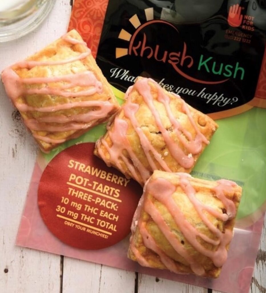 a photo of lightly browned square pastries with light pink frosting placed atop the khush kush packagin