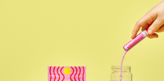 Cannabis-Infused Powdered Energy Drink Mix Launches: Vibations High + Energy neon yellow background display of pink drink mix container and weed nugs and a bottle of water with a white hand pouring pink drink mix into bottle