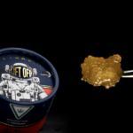 High Life Farms Launches New Line of BHO Extracts in Michigan product image black background lift off extracts container featuring an astronaut on the lid a chunk of golden wax is next to the container