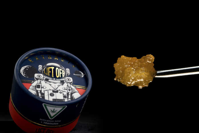 product image black background lift off extracts container featuring an astronaut on the lid a chunk of golden wax is next to the container