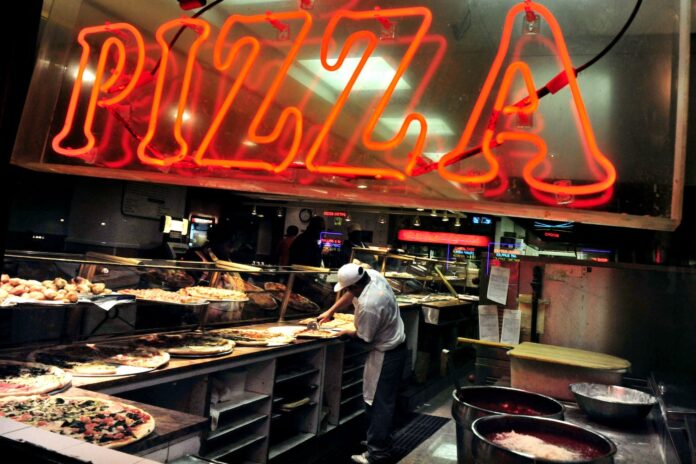 Red neon pizza sign above a man making pizzas at a shop