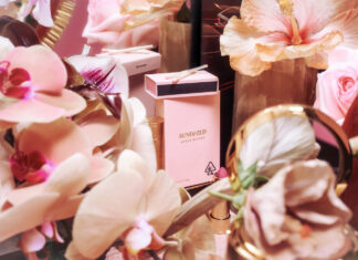 a light pink preroll box with a matching pack of matches surrounded by pink flowersh