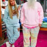 Camp High Launches Brand & Marketing Agency “Camp High Collective” a blonde woman and a man with a big white beard pose for a photo in their leisure sweatsuit line the woman is wearing a light blue sweatsuit and the man is wearing a pink and tie dye sweatsuit
