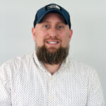 Hydra Unlimited Adds Senior Sales Staff a headshot of a man wearing a white button up a full brown beard and a dark blue baseball hat he is smiling and looking directly at the camera