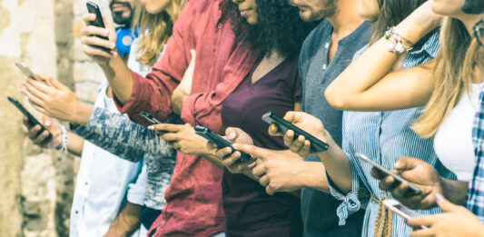 Group of multicultural friends using smartphone outdoors - People hands addicted by mobile smart phone - Technology concept with connected men and women - Shallow depth of field on vintage filter tone