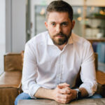 How to Acquire New Customers and Keep the Ones You Have man with beard in white business shirt with arms on table in brown leather chair kyle sherman flowhub