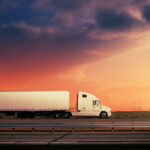 New Jersey Introduces Interstate Cannabis Commerce Bill White freight truck driving on freeway road under red sunset sky.