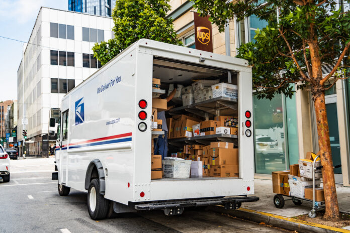 August 10, 2019 San Francisco / CA / USA - USPS delivery van stopped in front of a UPS location, unloading Amazon packages