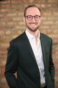 Cory-Rothschild-Headshot young professional in glasses and business attire