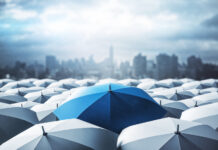 Identifying Key Tools to Survive an Economic Downturn Blue umbrella on top of other gray umbrellas on city background. Business and safety concept