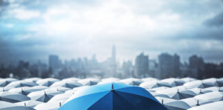 Identifying Key Tools to Survive an Economic Downturn Blue umbrella on top of other gray umbrellas on city background. Business and safety concept