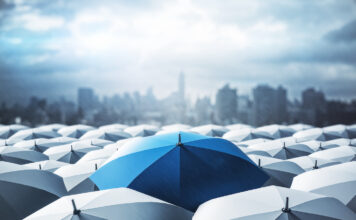 Identifying Key Tools to Survive an Economic Downturn Blue umbrella on top of other gray umbrellas on city background. Business and safety concept