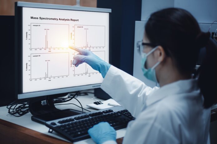 Scientist woman indicates the chromatogram of mass spectrometry analysis results of compounds, as shown on the computer monitor of mass spectrometer instrument in the laboratory for indoor vs outdoor cannabis study