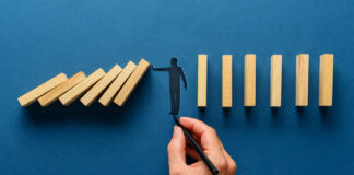 An Ounce of Prevention Can Stop Financial Distress Wide view image of male hand drawing silhouette of a man making a stop gesture to prevent wooden dominos from collapsing. Over navy blue background.