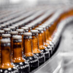 Tilray Triples Beverage Portfolio with $85M Anheuser-Busch Deal Beer bottles on conveyor production line. Brewery industry food factory manufacturing.