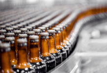 Tilray Triples Beverage Portfolio with $85M Anheuser-Busch Deal Beer bottles on conveyor production line. Brewery industry food factory manufacturing.