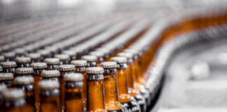 Tilray Triples Beverage Portfolio with $85M Anheuser-Busch Deal Beer bottles on conveyor production line. Brewery industry food factory manufacturing.