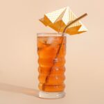 Glass of ice tea with decorative umbrella on beige background