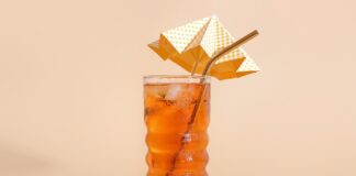 Glass of ice tea with decorative umbrella on beige background