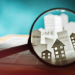 How to Navigate Retail Real Estate Magnifying glass in front of an open newspaper with paper houses. Concept of rent, search, purchase real estate.