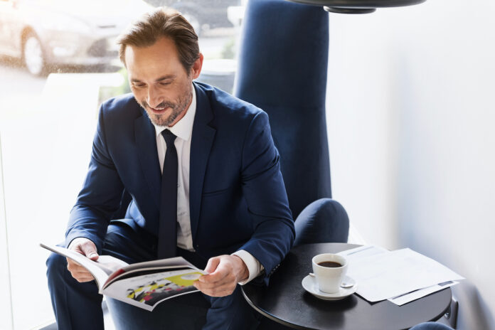 Businessman in suit reading magazine with morning coffee