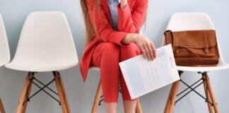 86% of Employers Plan to Hire More in 2024, but Benefits, DEI Declining young woman with modern red suit sitting for a job interview white chairs brown leather business bag