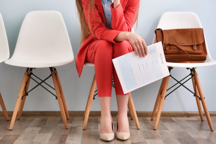 young woman with modern red suit sitting for a job interview white chairs brown leather business bag