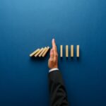 Thrive to Survive with Risk Mitigation Strategies for 2024 Top,View,Of,Businessman,Hand,Stopping,Falling,Dominos,In,A